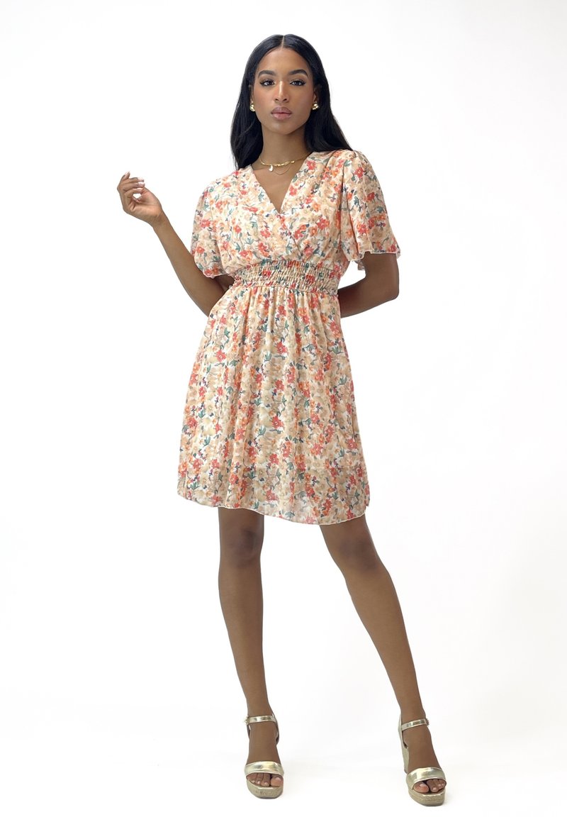 Robe florale en pêche clair avec des manches bouffantes courtes, une taille smockée et une jupe longueur genoux. Présente de petites fleurs multicolores et un tissu doux.
