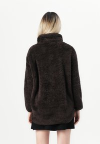Brun, plysch, översize fleecejacka med hög krage och långa ärmar, som har en mjuk textur och rundad nederkant.