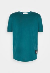 T-shirt corto teal a maniche corte in cotone, con collo rotondo, taglio dritto e una toppa con logo sul lato sinistro vicino all'orlo.