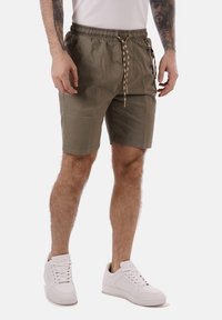 Bermuda khaki con coulisse e vita elastica, caratterizzati da una texture liscia e un design minimalista. Indossati con sneaker bianche.
