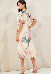 Vestido maxi floral con mangas cortas y con vuelo, colores pastel, fondo crema y detalle de lazo en la parte posterior. Tela suave y ligera.