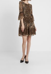 Leopardmönstrad klänning med långa utsvängda ärmar, figurnära midja och lager av kjol i bruna och svarta nyanser. Matchas med svarta högklackade skor.
