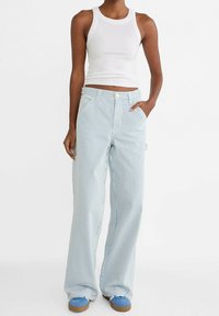 Pantalones de pierna ancha a rayas verticales en azul y blanco con cintura alta, un bolsillo frontal y cierre de botón. Combinados con una camiseta sin mangas blanca.