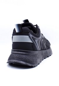 Chaussure de sport noire avec une semelle en caoutchouc texturé, un dessus en maille et des accents réfléchissants ; présente un design courbé et un soutien de cheville rembourré.