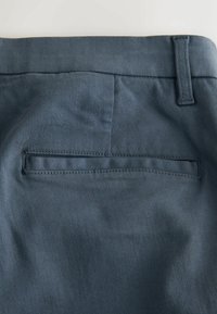 Sötétkék nadrág sima, texturált anyagból; hátul egy tisztán varrott szegéllyel ellátott nyílásos zseb található.