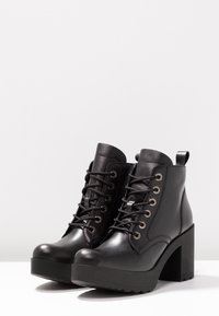 Black ankle boots made of smooth leather, featuring a chunky heel, round toe, lace-up design with metal eyelets, and a back pull tab.