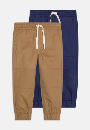 To sæt elastiske bukser: det ene i tan med en cremet snor og det andet i marineblå. Begge har tapered manchetter og subtile syninger.