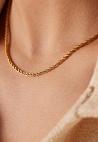 Goldene, gedrehte Kette mit glatter Textur, die auf der Haut ruht und eine Nahaufnahme ihrer Details und ihres Glanzes zeigt.