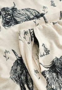 Țesătură de bumbac crem cu ilustrații negre cu o vacă, o rață și flori. Texturată, cu un aspect moale și drapat.