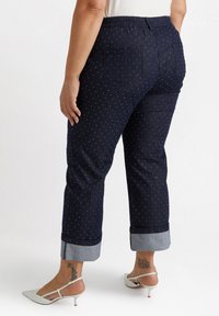 Marinblå denimbyxor med vita prickar, elastisk midja, bakfickor och uppvikta fållar som visar en ljusare denimkant.