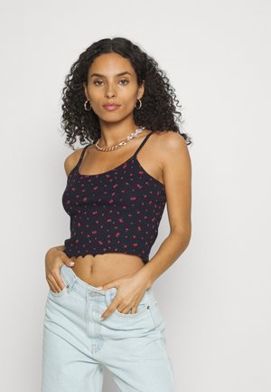 Top cropped azul-marinho com estampado floral vermelho, textura canelada, alças finas e um design de bainha ondulada, combinado com jeans azul-claro.