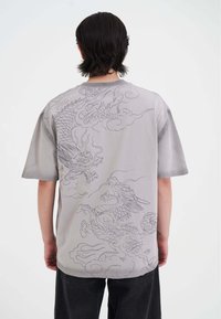 Camisa gris de manga corta con gráficos detallados de dragones en un gris más claro, con una textura suave y un corte relajado.