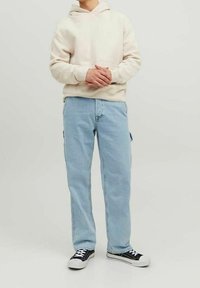 Ljusbeige hoodie med en framficka, tillsammans med ljusblå jeans och svarta sneakers med vita sulor. Avslappnad passform och stil.