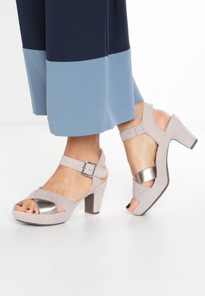 Grå ruskinds sandaletter med hæl og metalaccenter, åben tå, ankelrem med spænde og perforeret design foran. Gummisål.