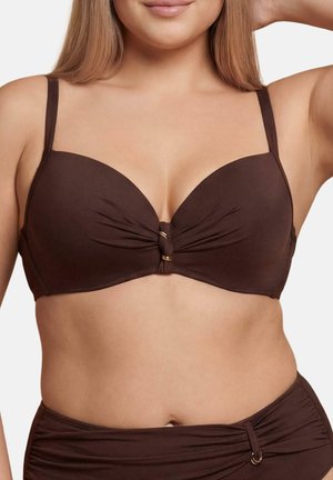 Kobieta w brązowym bikini z węzłem na środku góry i marszczonymi majtkami z wysokim stanem na jednolitym tle.