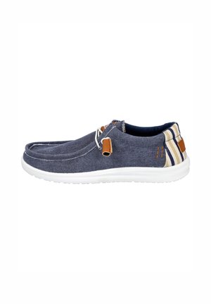 Zapato azul marino informal tipo slip-on con suela blanca, detalles en cuero marrón claro y detalle de tela a rayas en el talón.