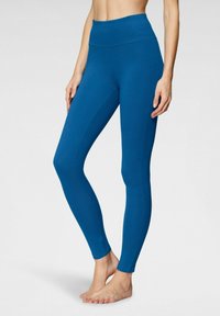 Leggings a vita alta in tessuto teal uniforme, caratterizzati da una texture liscia e un design aderente, che si estendono fino alla caviglia.