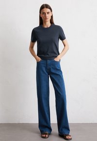 T-shirt navy a maniche corte con scollatura rotonda, abbinato a jeans in denim blu scuro a vita alta e sandali neri scivolati.