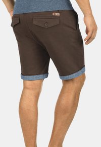 Shorts en coton marron avec des revers en denim, dotés de deux poches arrière avec boutons et d'un petit label de marque sur la ceinture.