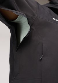 Chaqueta negra con un bolsillo con cremallera en el lado izquierdo, panel texturizado en los hombros y un forro interior de color azul claro.