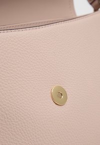 Borsa in pelle testurizzata rosa chiaro con un dettaglio circolare in metallo dorato sulla parte anteriore, che migliora il suo design moderno.