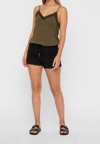 Oliwkowa zielona bezrękawna bluzka z dekoltem w kształcie litery V oraz czarne koronkowe szorty z falowanym wykończeniem. Całość dopełniają czarne sandały.