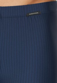 Marinblå simshorts med ribbat mönster, som har en svart "SCHIESSER"-etikett på midjebandet för varumärkesidentifiering.