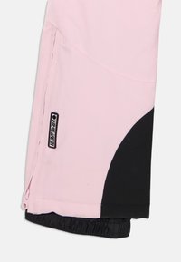 Rožinės ir juodos slidinėjimo kelnės, pagamintos iš minkštos, tvirtos medžiagos. Yra šoninis užtrauktukas, elastinga juostos dalis ir logotipo ženklelis. Lygi tekstūra, spalvų blokų dizainas.