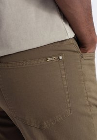 Pantalon en coton marron avec une poche arrière ornée d'une étiquette en métal gravée "OMBRE DEPT." et un accent de bouton argenté.