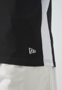Camiseta de manga corta en blanco y negro con dobladillo curvado, que presenta un pequeño logotipo blanco en el lado. La tela parece suave, con una textura de mezcla de algodón.