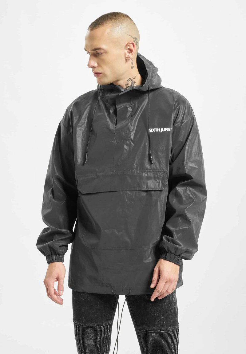 Svart vanntett anorakk med halv-zip foran, elastiske ermer, justerbar snor i kanten og frontlomme; har trykt logo på brystet.