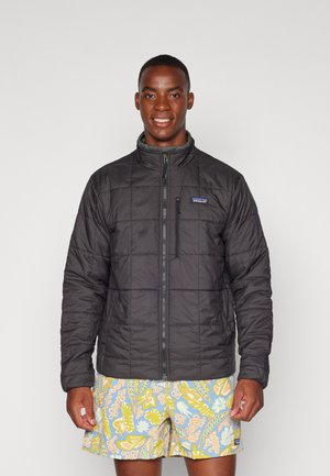 Zwarte geïsoleerde pufferjack met een rits aan de voorkant, staande kraag en gestikte patronen. Gecombineerd met meerkleurige bloemen zwemshorts.