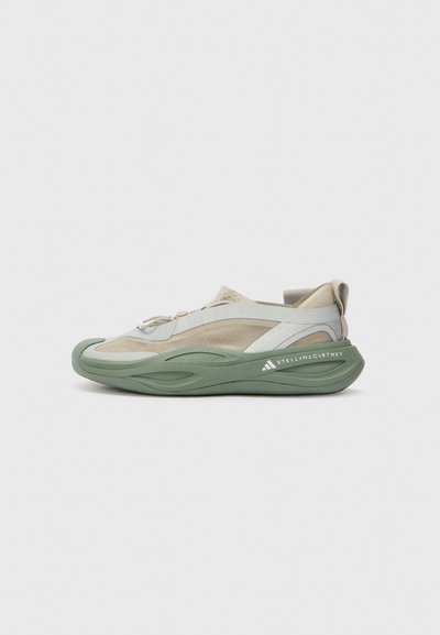 Sportschuhe mit einer grünen Gummisohle, einem hellgrauen Mesh-Obermaterial und beigen Akzenten. Verfügt über ein aerodynamisches Design und ein elastisches Schnürsystem.
