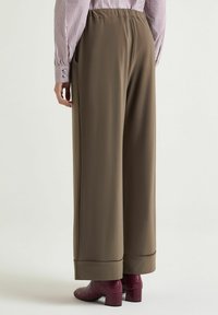 Pantaloni a gamba larga verde oliva con vita elastica e tasche laterali, abbinati a stivali con tacco bordeaux dalla texture lavorata.
