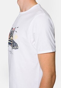 Biała bawełniana koszulka z kolorowym nadrukiem przedstawiającym klasyczny samochód, palmy i ptaki. Klasyczny okrągły dekolt i krótkie rękawy.