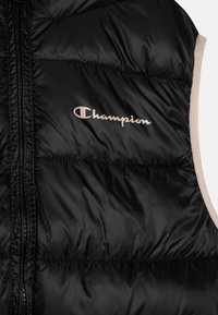 Czarna kamizelka puchowa o gładkiej, błyszczącej teksturze, z zamkiem błyskawicznym i beżowym wykończeniem. Logo "Champion" jest wytłoczone w srebrnym kolorze z przodu.