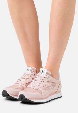Sneaker rosa chiaro realizzate in suede e mesh con un tallone bianco, caratterizzate da un logo sulla linguetta, lacci rotondi e una suola in gomma nera.