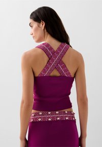 Top aderente viola con spalline incrociate, caratterizzato da un motivo di maglia testurizzata. Sul retro presenta un'apertura a fessura e dettagli decorativi.