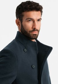 Cappotto di lana blu scuro con colletto alto, design doppiopetto e bottoni neri. Caratterizzato da una texture elegante e una silhouette strutturata.