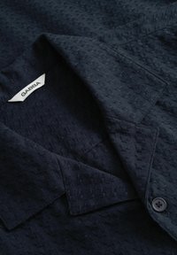 Mørk marineblå teksturert blazer med hakket krage, lukkes med én knapp, og GABBA-merke inne i kragen.