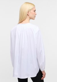 Hvid langærmet bluse med en afslappet pasform, rund halsudskæring og sammenkrøllet detaljering bagpå. Har knaplukning ved ærmerne og slidser i siderne.
