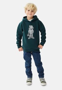 Turkos huvtröja med björngrafik och hörlurar; kombinerad med blå jeans och gröna sneakers; slät textur; avslappnad passform.