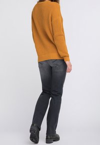 Sinapinkeltainen neulepaita rentoa istuvuutta, ribbereidyillä hihoilla, yhdistetty tummanharmaisiin farkkuihin ja mustiin nauhakengiin.