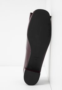 Burgundské lakované kožené boty na podpatku s hladkým povrchem, kulatou špičkou a černou gumovou podrážkou. Čisté linie a jednoduchý design.