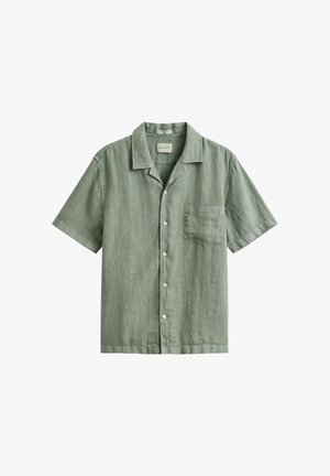Camisa de lino de manga corta en verde salvia con botones al frente, un bolsillo en el pecho y un cuello relajado, colocada sobre un fondo blanco.