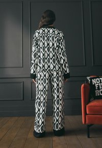 Set de pijamale alb-negru cu un model ce prezintă desene stilizate ale mâinilor pe un material asemănător satinului. Croială lejeră cu manșete și brâu negru.