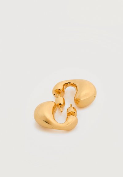 Ζευγάρι λαμπερών, χοντρών χρυσών κρίκων αυτιών με κλεισίματα τύπου κούμπωμα σε λευκό φόντο.