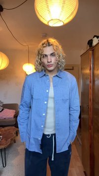 Niebieska koszula w kratę z guzikami, lekki materiał, noszona na białej koszulce na ramiączkach, w połączeniu z ciemnymi spodniami dresowymi; miękki, casualowy tekstur.