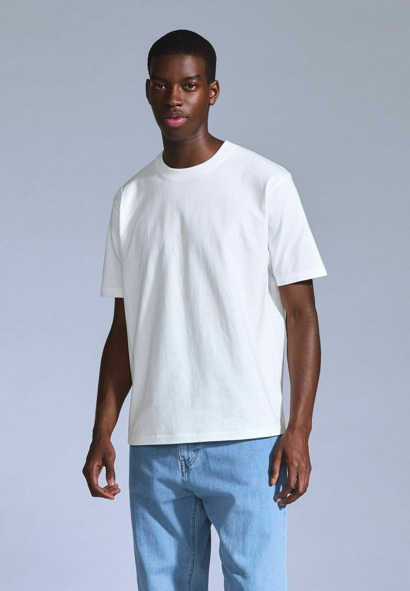 White cotton T-shirt with short sleeves and a crew neckline, paired with light blue denim jeans, displayed against a neutral background.