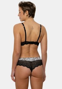 Ensemble de lingerie en dentelle noire avec un design à bords festonnés, orné de délicates fleurs sur la ceinture et de bretelles réglables sur le soutien-gorge.